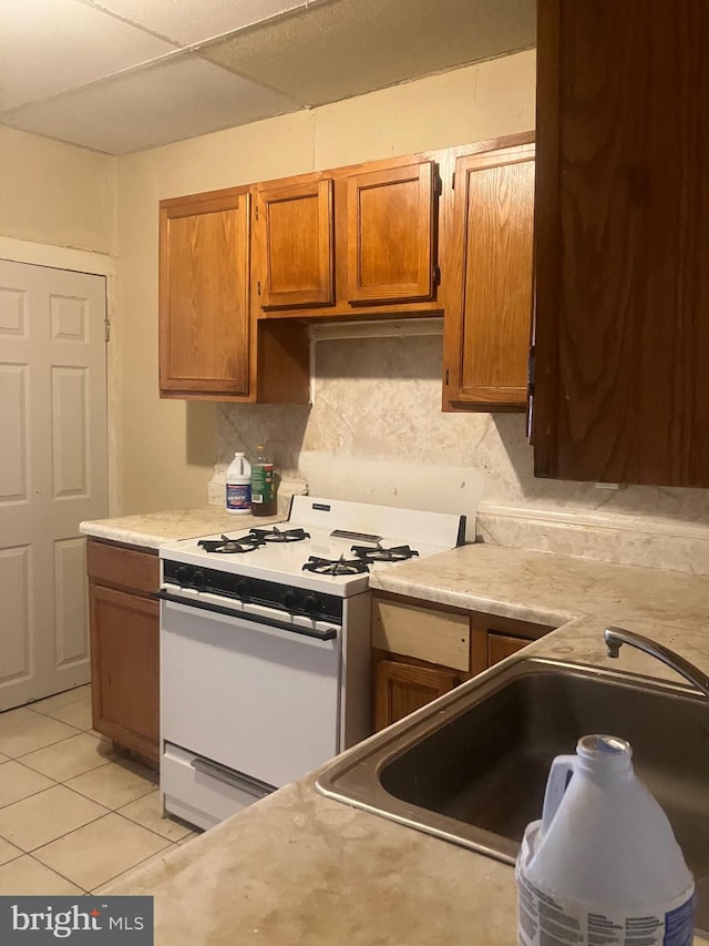 kitchen featuring backsplash, white range with gas cooktop, sink, and light tile patterned flooring