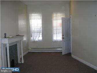 unfurnished living room with a fireplace and a baseboard heating unit