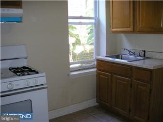 kitchen with light tile patterned flooring, sink, white range with gas cooktop, and exhaust hood