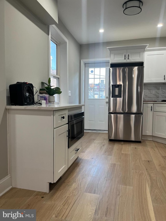 kitchen with tasteful backsplash, white cabinetry, appliances with stainless steel finishes, and light hardwood / wood-style flooring