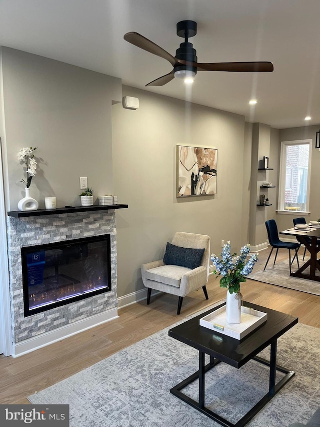 living room with hardwood / wood-style floors, ceiling fan, and a stone fireplace