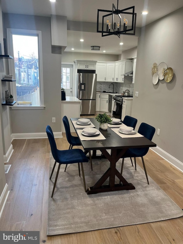 dining space featuring sink, light wood-type flooring, and a notable chandelier