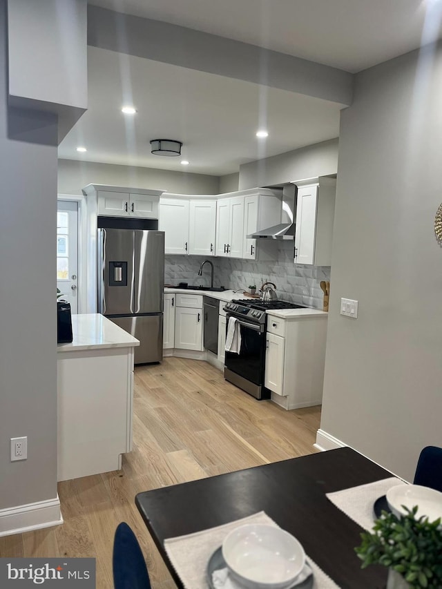 kitchen with white cabinetry, sink, wall chimney exhaust hood, appliances with stainless steel finishes, and light wood-type flooring