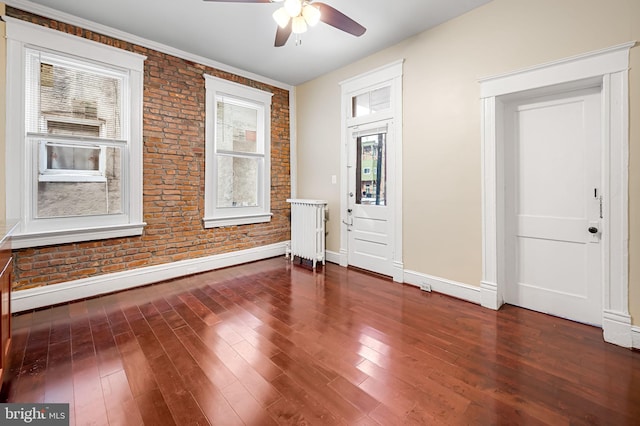 unfurnished room with ceiling fan, plenty of natural light, brick wall, and radiator