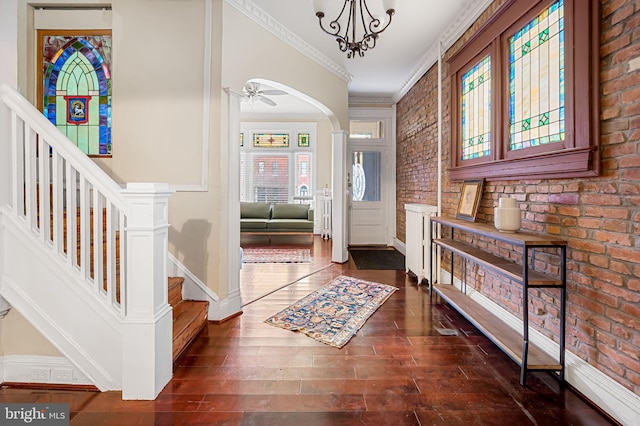 entryway with crown molding, dark hardwood / wood-style flooring, brick wall, and ceiling fan with notable chandelier