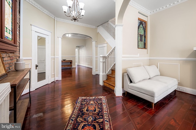 sitting room with ornate columns, crown molding, dark wood-type flooring, and a notable chandelier