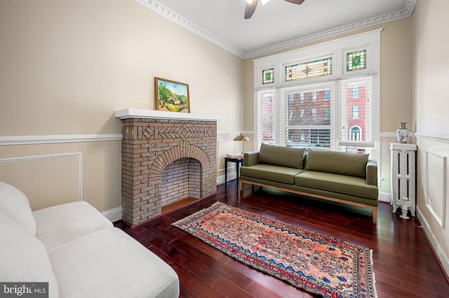 living room featuring dark hardwood / wood-style floors, a brick fireplace, ceiling fan, and ornamental molding