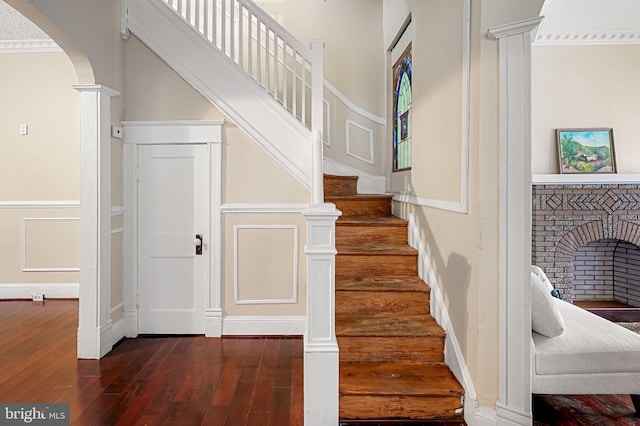 stairway featuring wood-type flooring, ornamental molding, a fireplace, and decorative columns