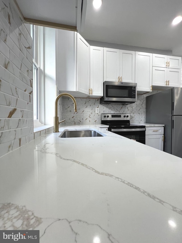 kitchen with light stone countertops, white cabinets, sink, and stainless steel appliances