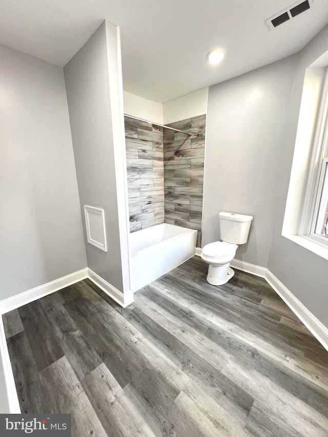 bathroom with tiled shower / bath combo, hardwood / wood-style flooring, and toilet