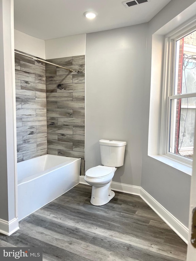 bathroom with tiled shower / bath, hardwood / wood-style flooring, and toilet