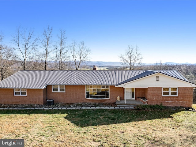 back of property with a lawn, a mountain view, and central AC unit