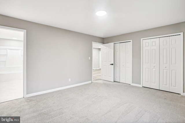 unfurnished bedroom featuring light colored carpet, connected bathroom, and two closets