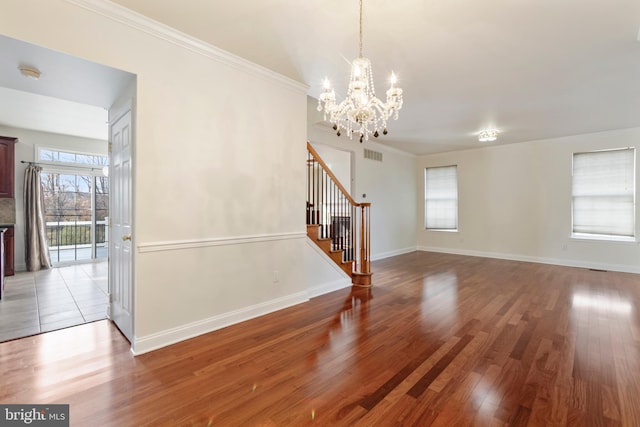 unfurnished living room featuring hardwood / wood-style flooring, a notable chandelier, and ornamental molding