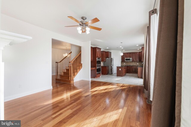 unfurnished living room featuring ceiling fan with notable chandelier and light wood-type flooring