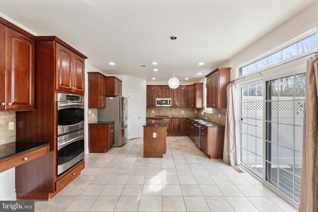 kitchen featuring appliances with stainless steel finishes, tasteful backsplash, a kitchen island, hanging light fixtures, and light tile patterned flooring