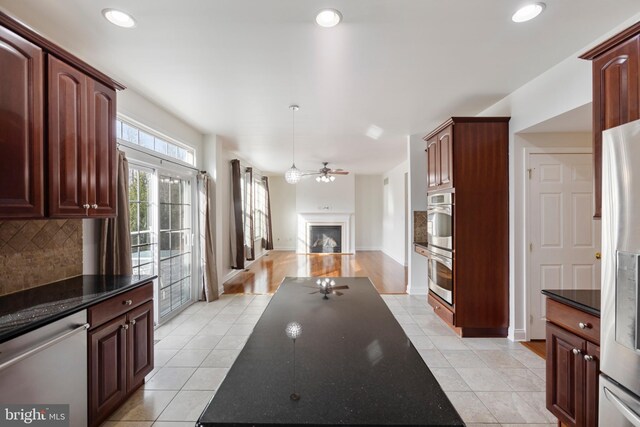 kitchen featuring decorative backsplash, stainless steel appliances, ceiling fan, pendant lighting, and dark stone countertops