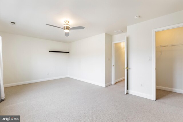 unfurnished bedroom with ceiling fan, light colored carpet, a walk in closet, and a closet