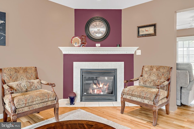 sitting room with wood-type flooring, ceiling fan, and a tile fireplace