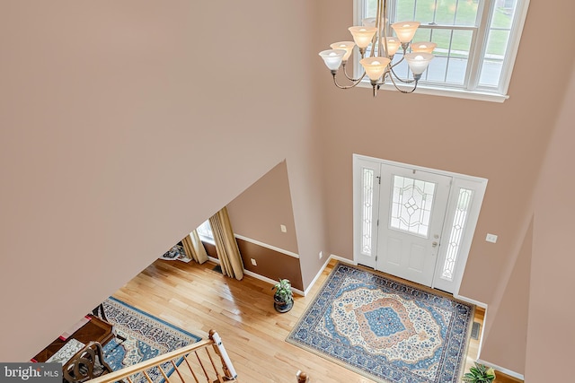 entrance foyer featuring an inviting chandelier, hardwood / wood-style floors, a healthy amount of sunlight, and a towering ceiling