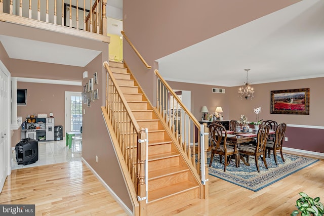 staircase featuring wood-type flooring, crown molding, and a notable chandelier