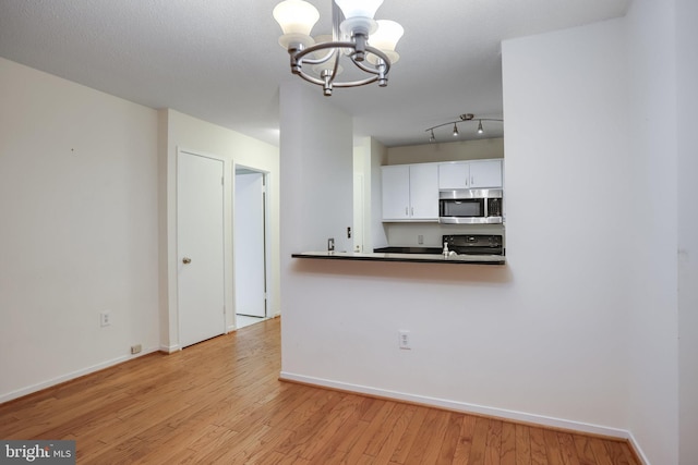 kitchen with white cabinetry, black range oven, a notable chandelier, kitchen peninsula, and light wood-type flooring