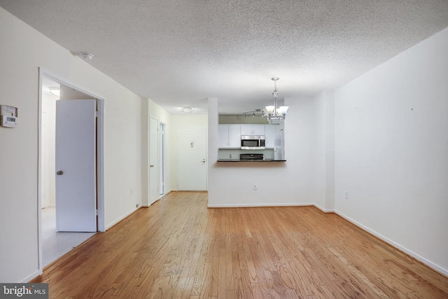 unfurnished living room featuring a textured ceiling, light hardwood / wood-style floors, and a notable chandelier