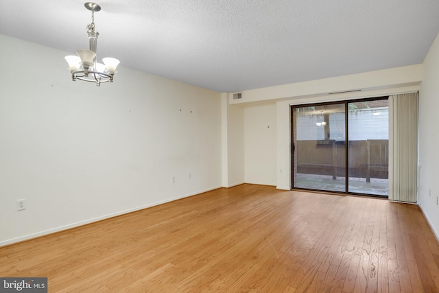 spare room with light hardwood / wood-style floors, a textured ceiling, and a notable chandelier