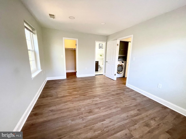 unfurnished bedroom featuring a spacious closet, dark wood-type flooring, washer / dryer, and a closet