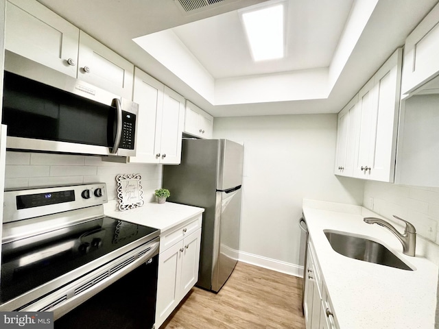 kitchen featuring stainless steel appliances, light hardwood / wood-style floors, sink, a raised ceiling, and white cabinetry