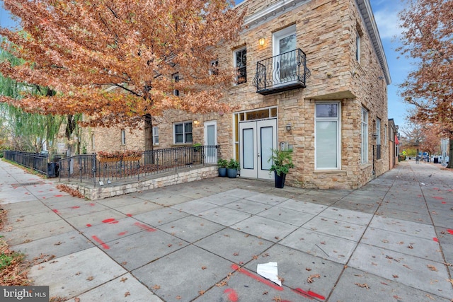 back of property with french doors, stone siding, a patio, and a balcony