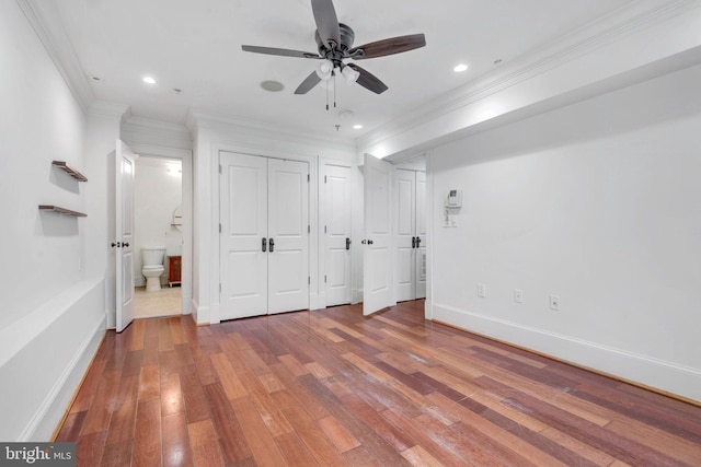 unfurnished bedroom with two closets, wood finished floors, ornamental molding, baseboards, and ensuite bathroom