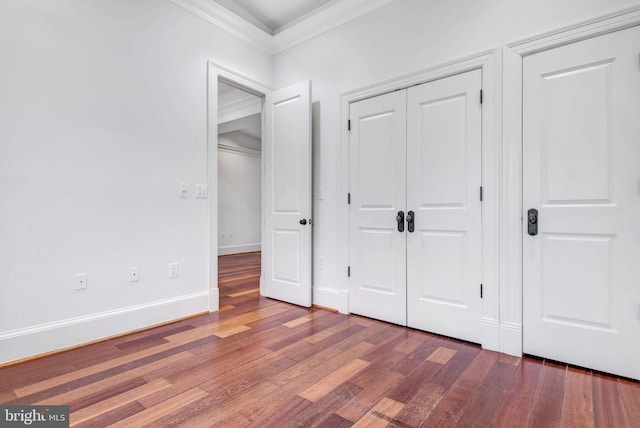unfurnished bedroom with ornamental molding, wood finished floors, a closet, and baseboards