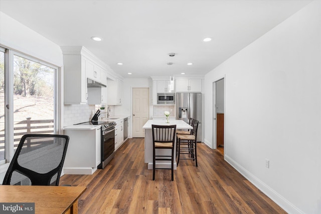 kitchen with white cabinets, a kitchen island, stainless steel appliances, and dark wood-type flooring