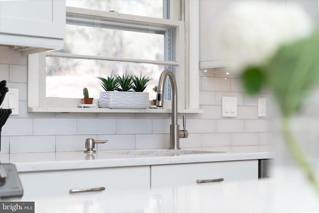 interior details with white cabinets, tasteful backsplash, and light stone countertops