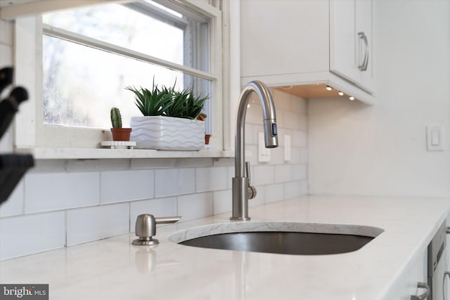 interior details featuring white cabinets, decorative backsplash, light stone countertops, and sink