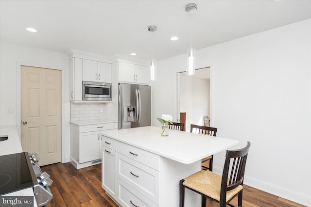 kitchen with a breakfast bar, dark wood-type flooring, hanging light fixtures, appliances with stainless steel finishes, and white cabinetry