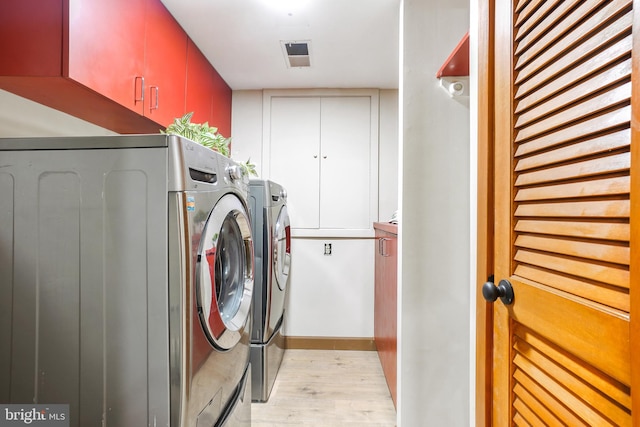 laundry room featuring light hardwood / wood-style floors, cabinets, and washing machine and dryer