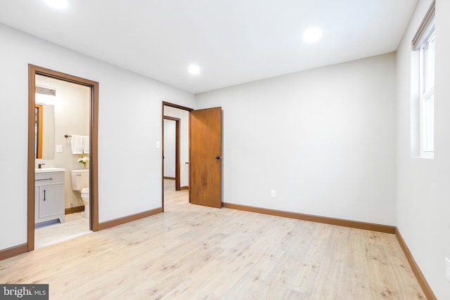 unfurnished bedroom featuring multiple windows, light hardwood / wood-style floors, and connected bathroom