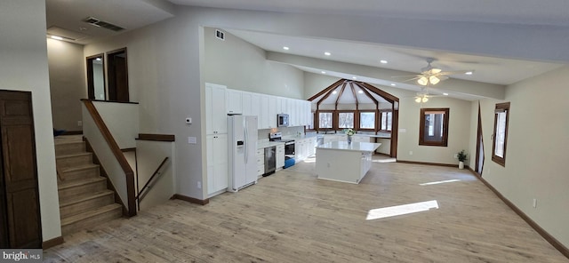 kitchen with white cabinets, lofted ceiling, light wood-type flooring, a kitchen island, and appliances with stainless steel finishes