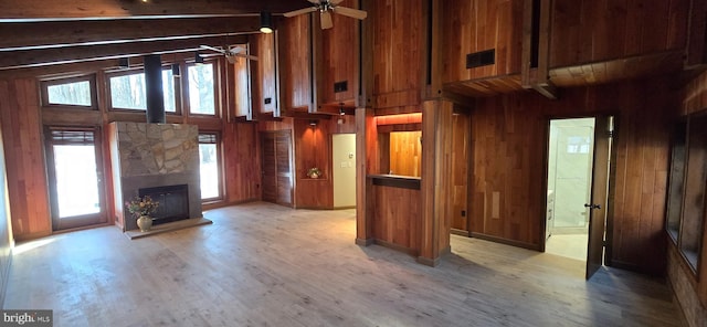 unfurnished living room with light hardwood / wood-style flooring, wooden walls, a towering ceiling, ceiling fan, and a stone fireplace