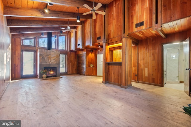 unfurnished living room featuring wooden ceiling, a towering ceiling, light hardwood / wood-style floors, wood walls, and a stone fireplace