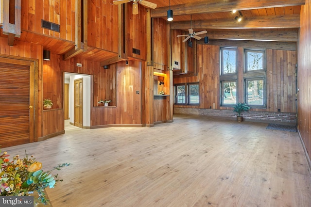 unfurnished living room featuring wooden ceiling, beamed ceiling, ceiling fan, light wood-type flooring, and wood walls