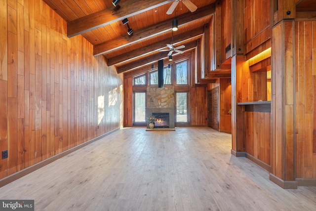 unfurnished living room with a stone fireplace, wooden walls, high vaulted ceiling, and rail lighting