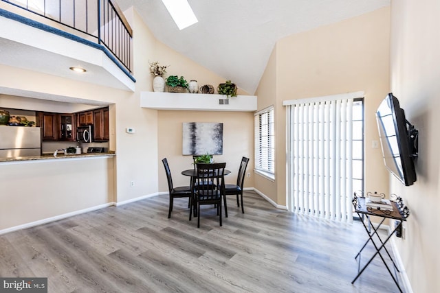 dining room featuring a skylight, high vaulted ceiling, and light hardwood / wood-style flooring