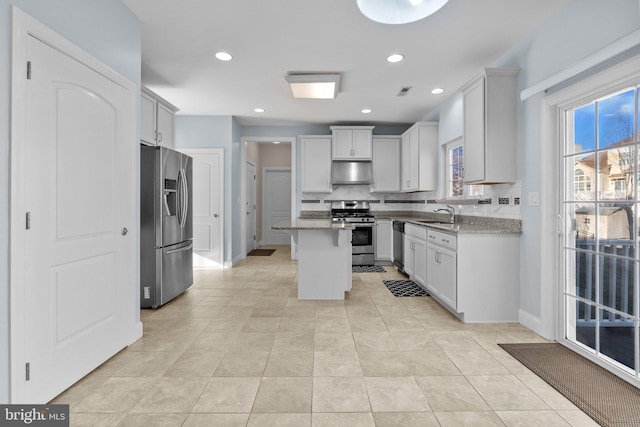 kitchen with white cabinetry, appliances with stainless steel finishes, light stone countertops, a kitchen island, and decorative backsplash