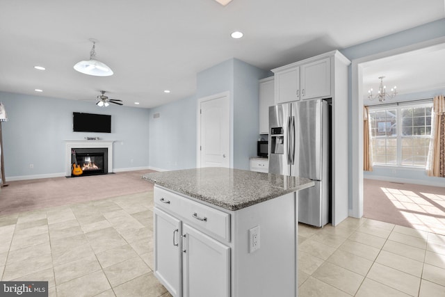 kitchen with ceiling fan with notable chandelier, a center island, stainless steel refrigerator with ice dispenser, light stone countertops, and white cabinetry