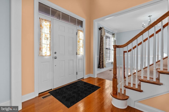 entrance foyer with ornamental molding, wood-type flooring, and a notable chandelier