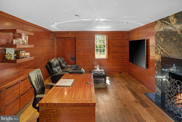 office area featuring a high end fireplace, wooden walls, and light hardwood / wood-style flooring