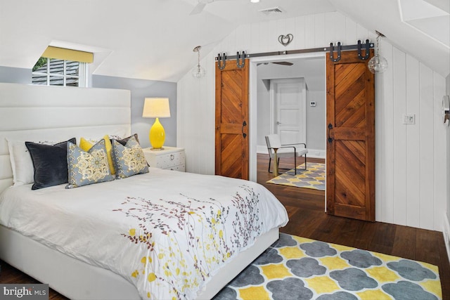 bedroom with dark hardwood / wood-style flooring, lofted ceiling, a barn door, and wooden walls